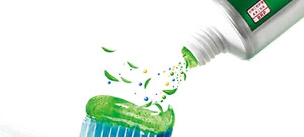 A toothpaste tube with aloe vera extract being applied to a toothbrush, emphasizing oral health benefits.